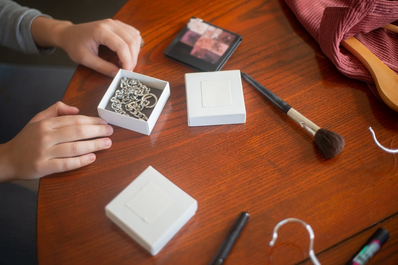 Close-up of jewelry and makeup accessories on a wooden table, including a necklace and makeup brush.